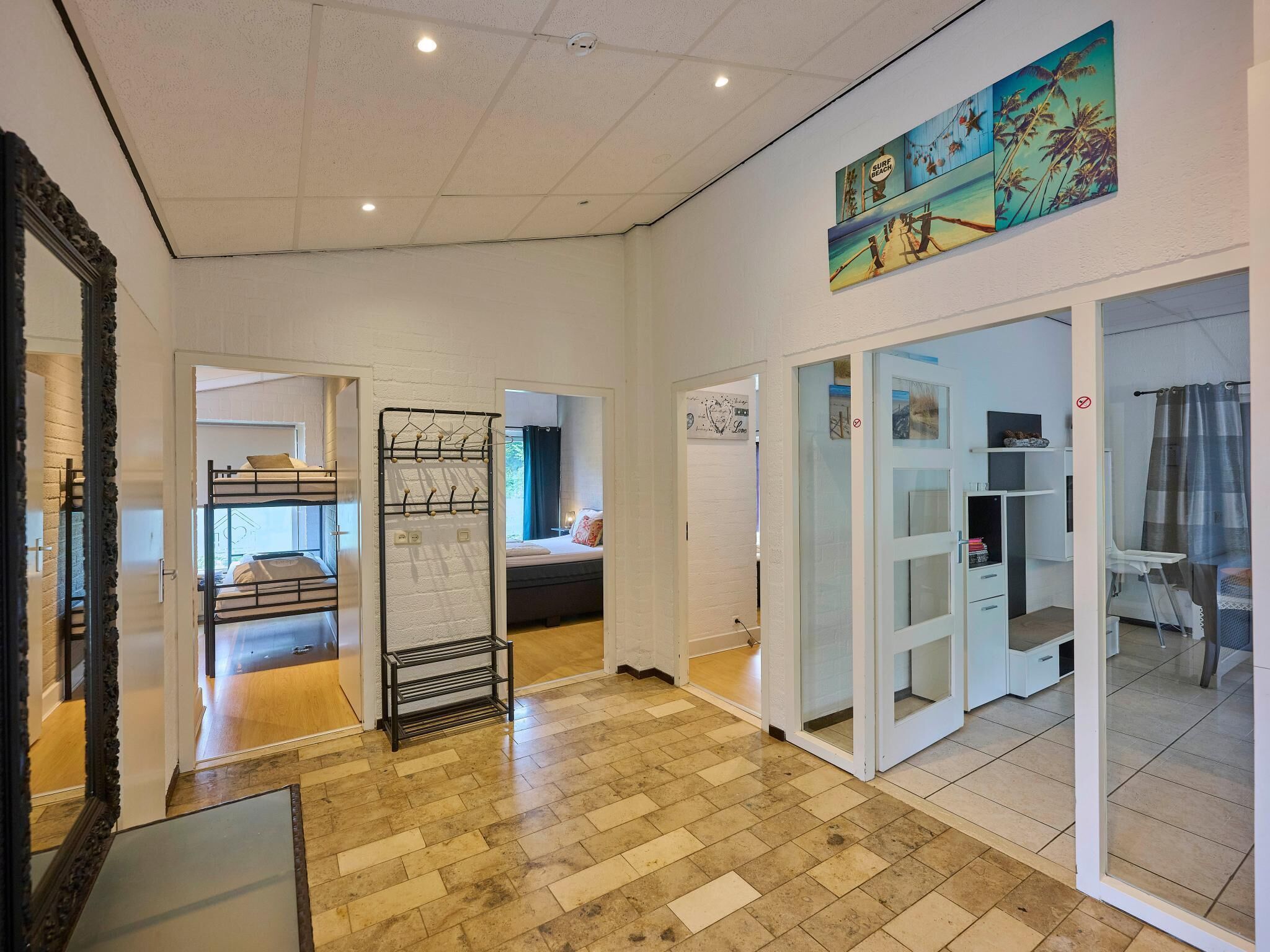 A hotel room with a bunk bed, a drying rack, a glass door leading to a bathroom, and a large window with a view of palm trees.