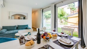 A modern living room with a sofa, dining table set with wine glasses, a bottle, and fruit. - La Porte Rouge 100 Mt From Lake Maggiore (Meina)