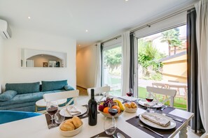 Ein modernes Wohnzimmer mit einer Couch, einem Esstisch, Weingläsern, einer Flasche und Obst.