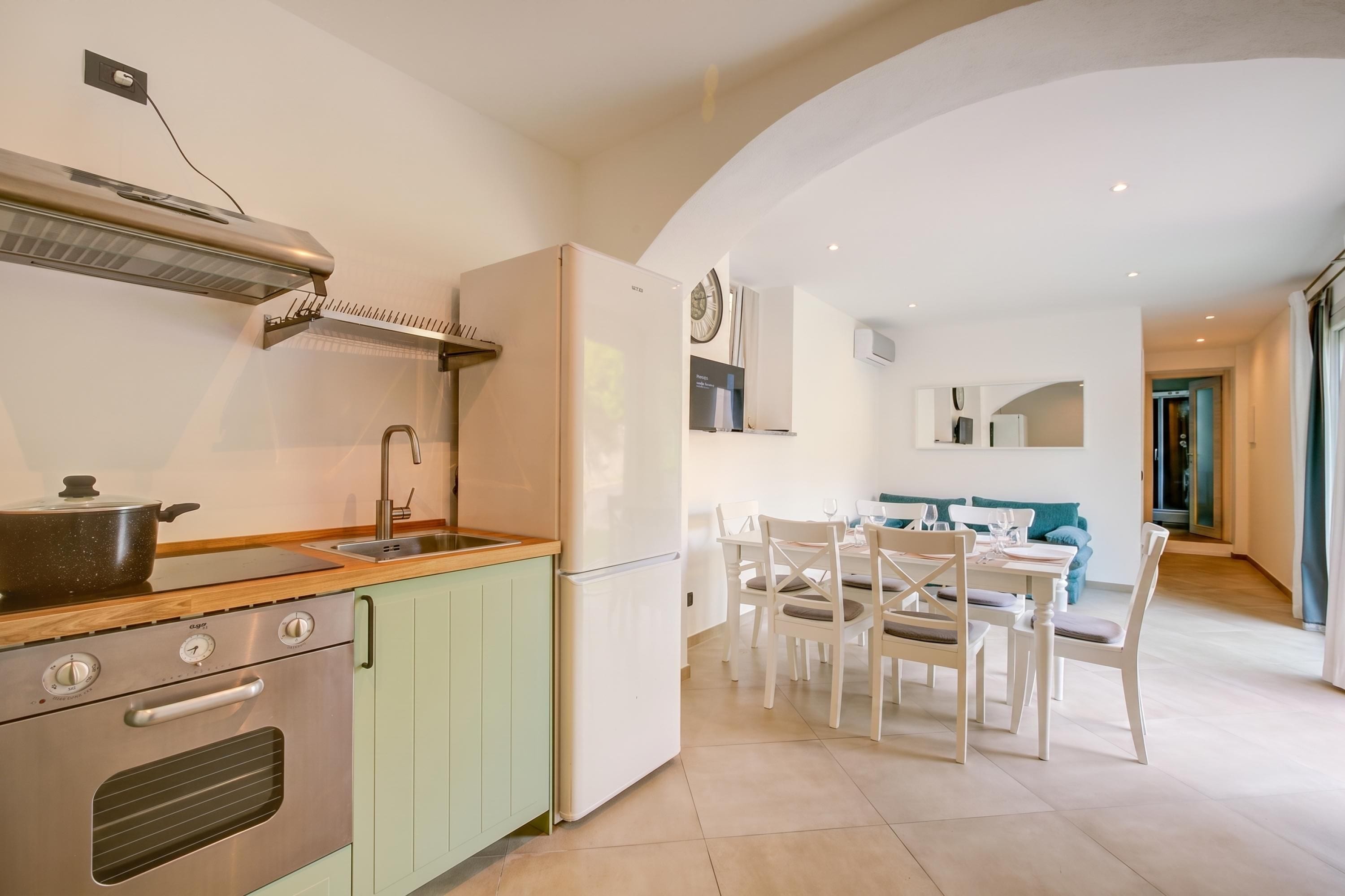 Une cuisine compacte équipée d’une cuisinière, d’un évier et d’un réfrigérateur, qui donne sur un coin repas avec une table et des chaises.