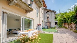 A patio with a table set for breakfast, a covered outdoor seating area, and a building with a stone facade. - La Porte Rouge 100 Mt From Lake Maggiore (Meina)
