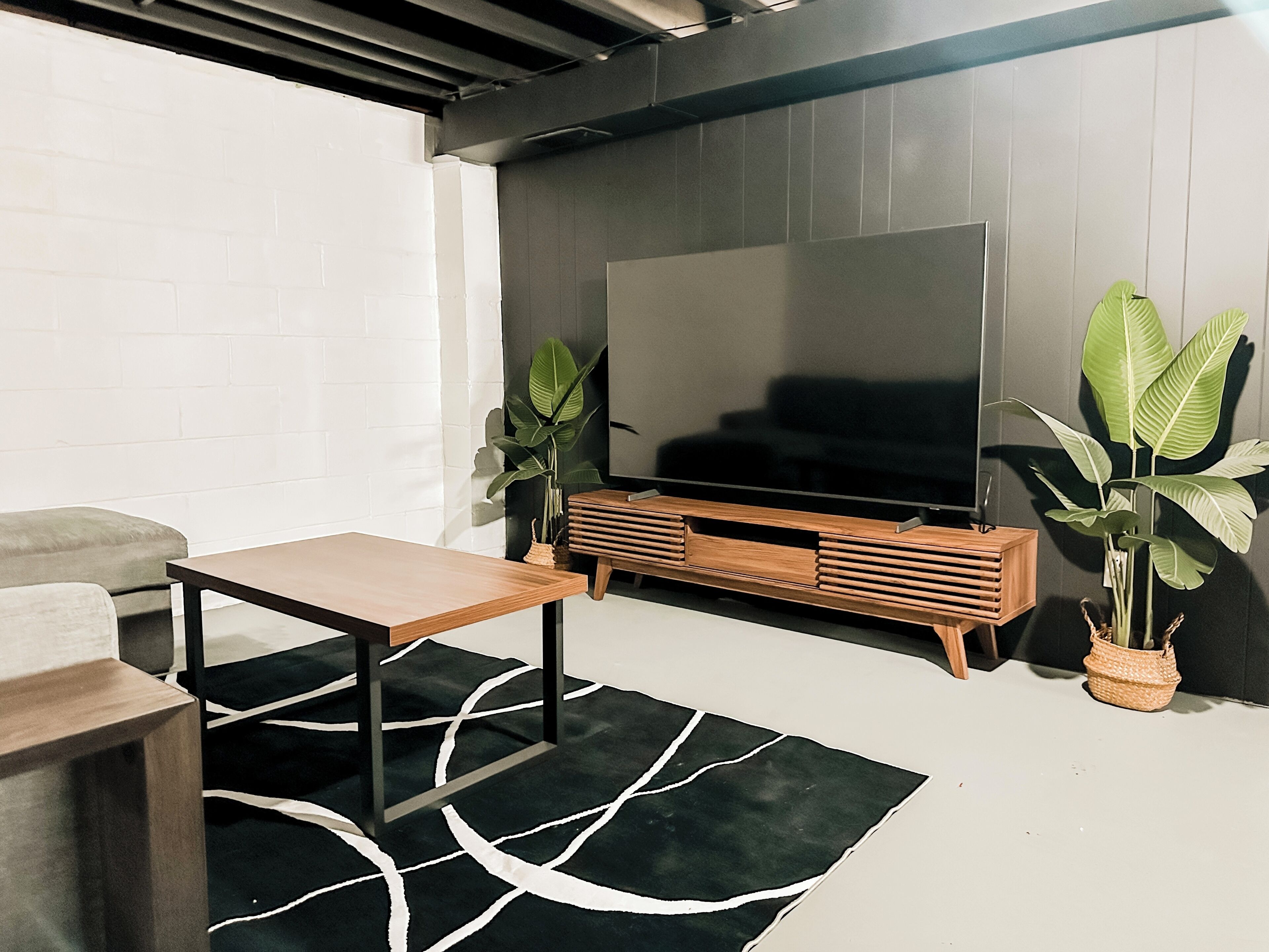 Una sala de estar moderna con un televisor de pantalla plana, un mueble de madera para entretenimiento, una mesa de centro y dos plantas en macetas.