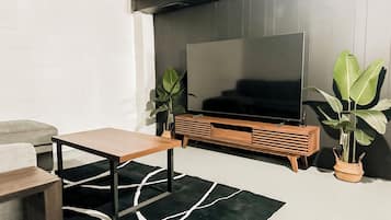 Una sala de estar moderna con un televisor de pantalla plana, un mueble de madera para entretenimiento, una mesa de centro y dos plantas en macetas.