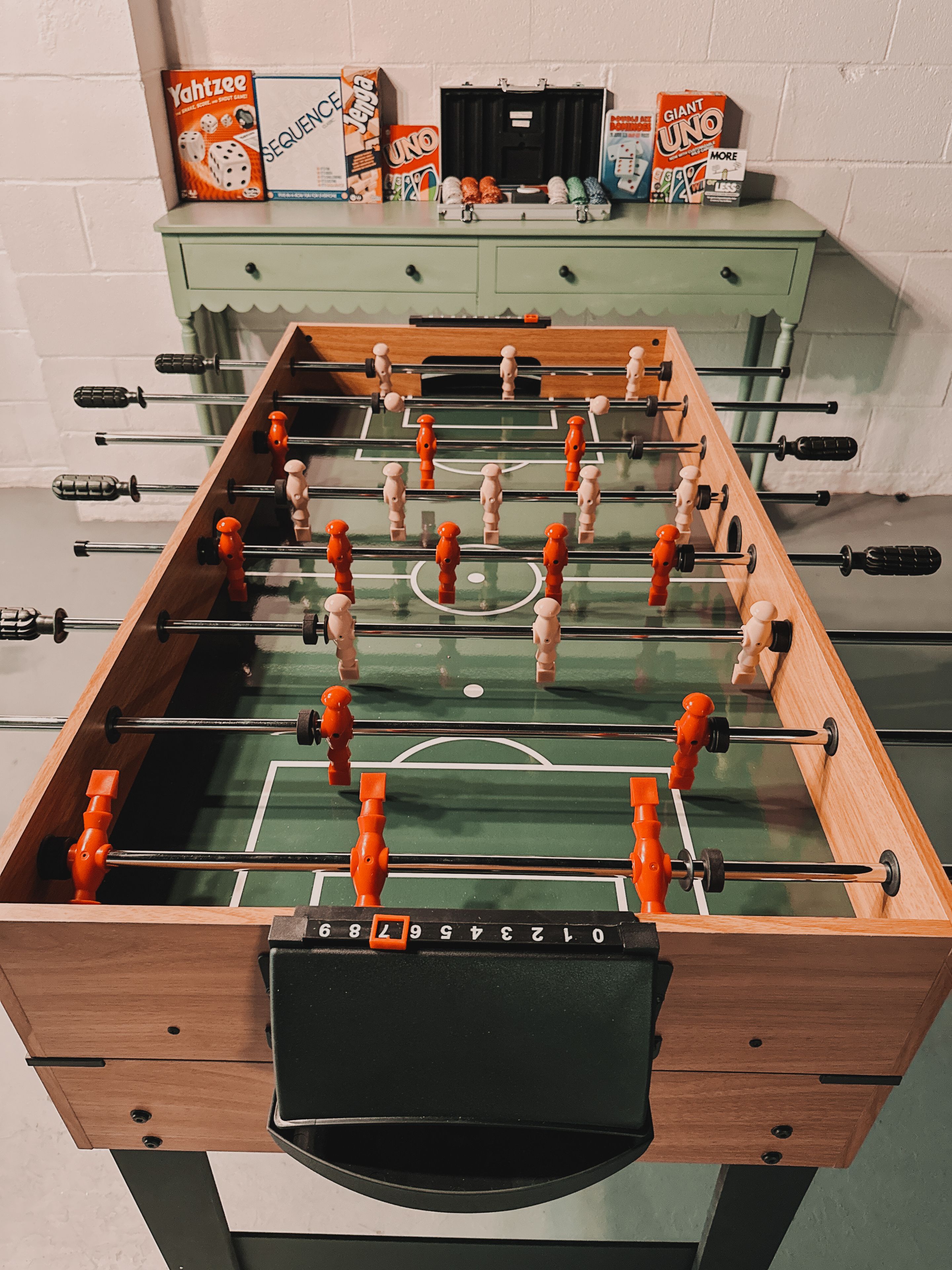 Ein Kicker mit Holzrahmen und orangenen Griffen vor einer weißen Ziegelwand.
