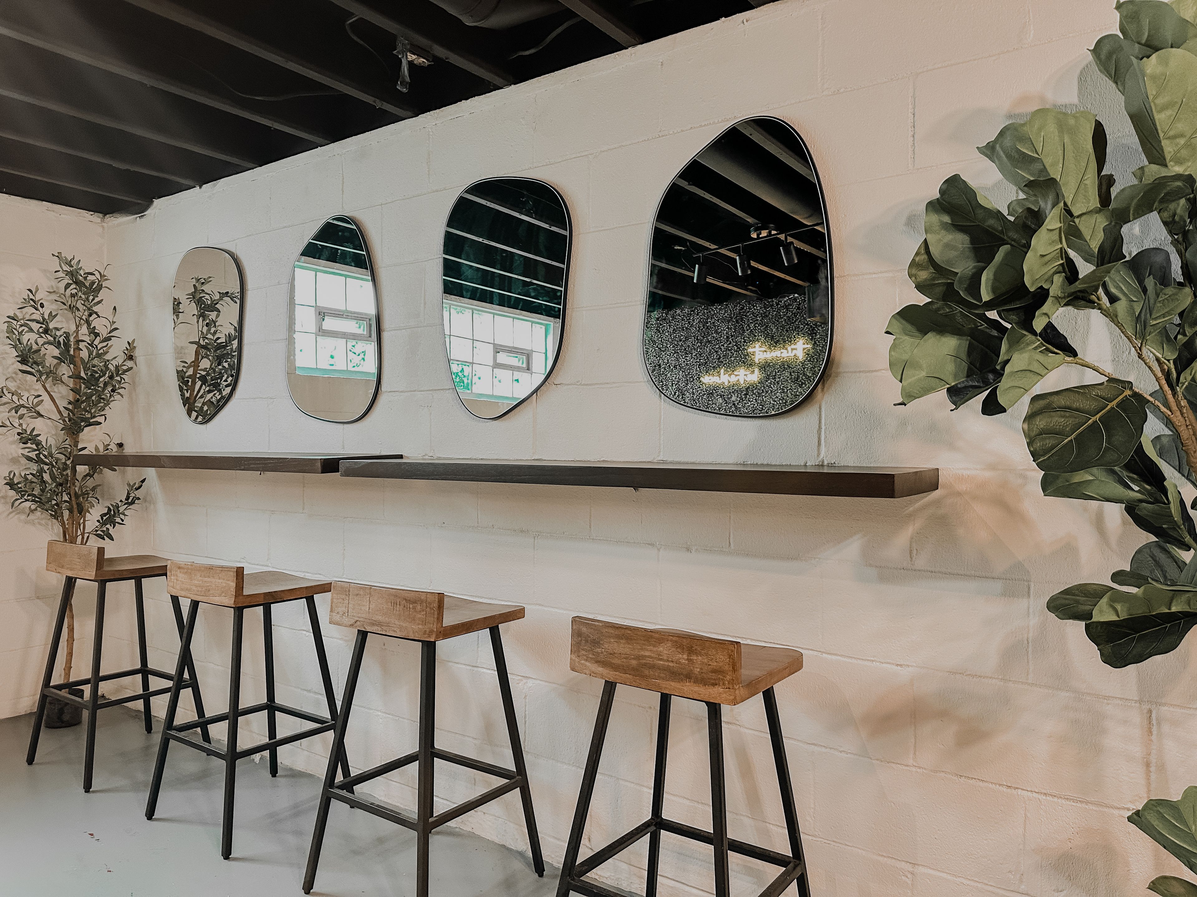 Zona de bar con tres espejos, taburetes de madera y una planta en maceta.