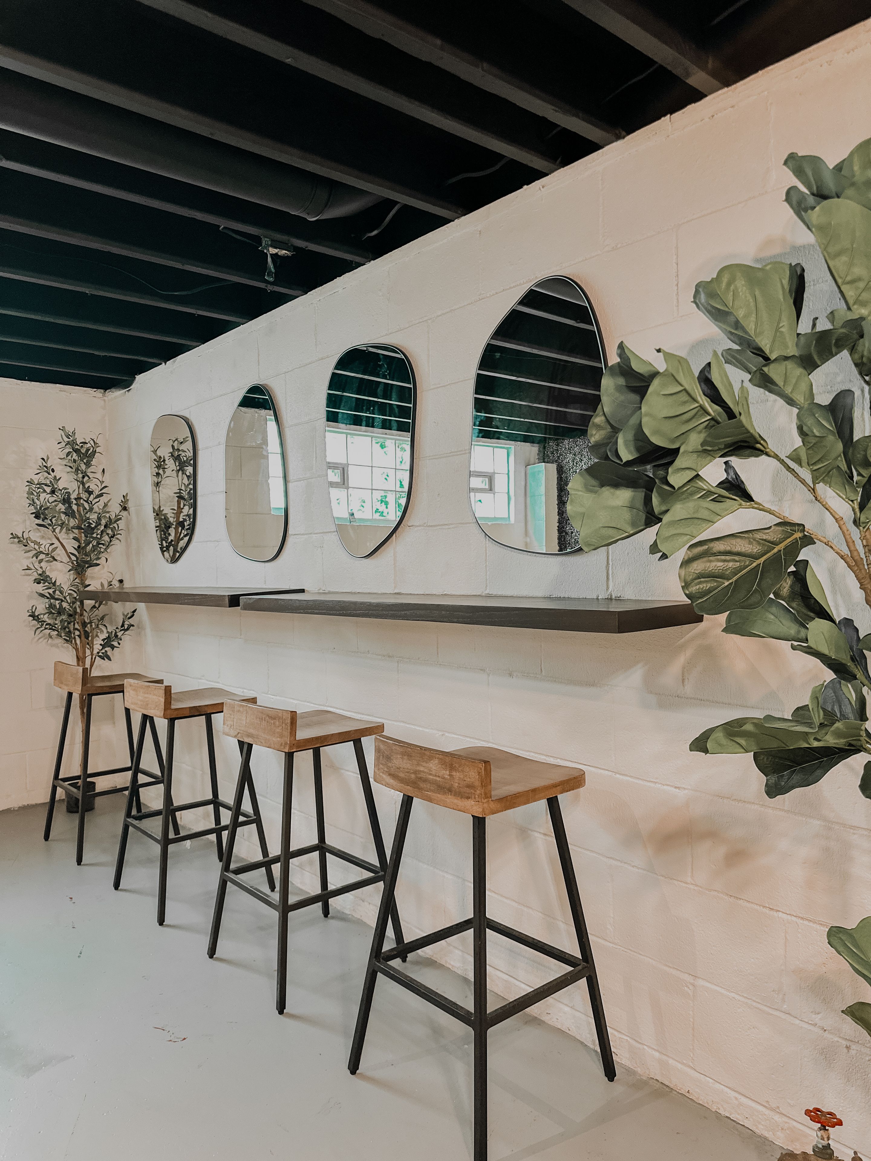 Un espace bar comprenant trois tabourets, un comptoir et trois miroirs fixés au mur.