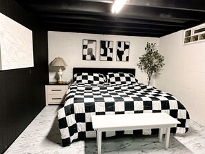 Een slaapkamer met een geruit beddegoed, een nachtkastje met een lamp, en een aan de muur hangend kunstwerk.