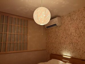 Una stanza con un letto, una finestra con persiane a griglia, un condizionatore d'aria fissato al muro e un lampadario.