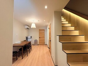 Ein modernes Interieur mit einer Holztreppe, einem Essbereich mit Tisch und Stühlen sowie einer Küchenzeile mit Geräten.