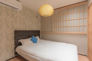 Ein Schlafzimmer mit einem Bett, einem Fenster mit Rasteroptik und einer Pendelleuchte.