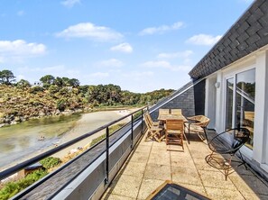 Eine Terrasse mit Blick auf einen Fluss, Gartenmöbel und einem Geländer.