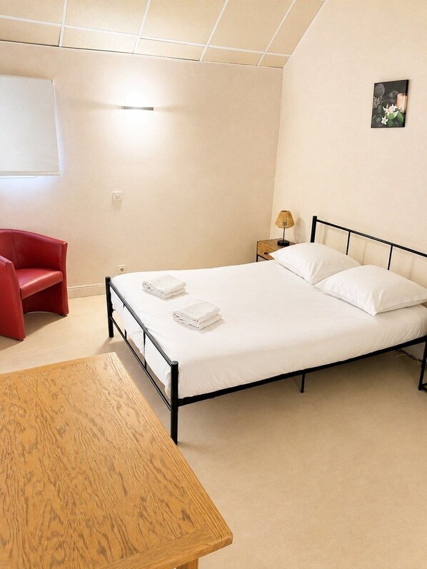 Ein Hotelzimmer mit einem Bett, einem roten Sessel, einem Holztisch und einem Nachttisch mit Lampe.