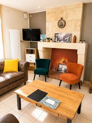 Ein Wohnzimmer mit Kamin, Fernseher und Sitzgelegenheiten, darunter ein Sofa und zwei Sessel.