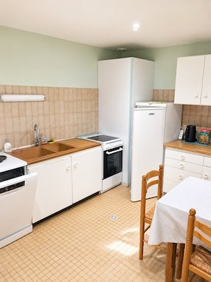 Une cuisine compacte comprenant un évier, une cuisinière et un réfrigérateur, une table à manger avec des chaises et un sol carrelé.