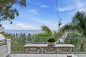 A balcony with a table and chairs, overlooking a coastal view with a crane in the distance. - Burleigh Vista, Burleigh Heads (Burleigh Heads)