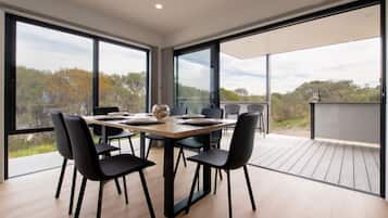 A modern dining area with a large table and chairs, large windows, and a view of the outdoors.