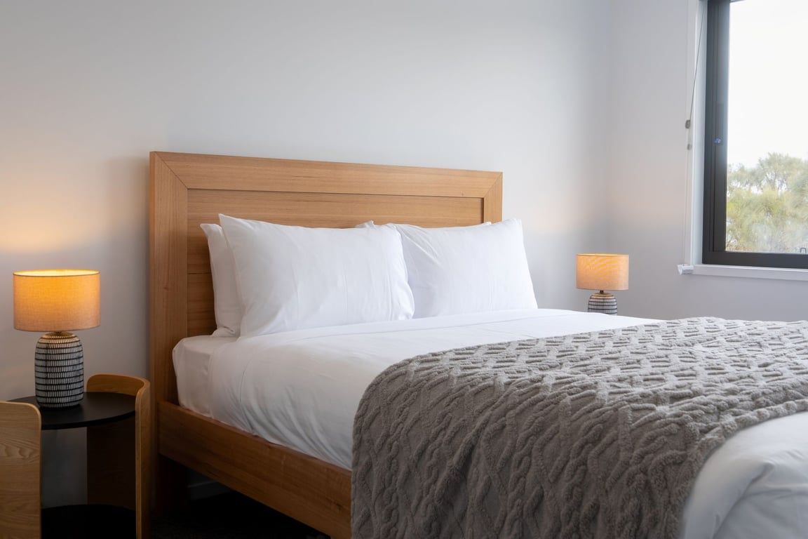 A neatly made bed with a wooden headboard, two bedside lamps, and a window with a view.