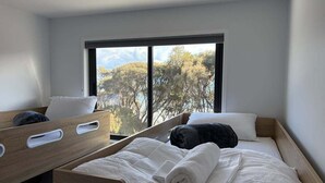 Ein Schlafzimmer mit großem Fenster, einem Bett mit weißer Bettwäsche und einem Holzkopfteil.