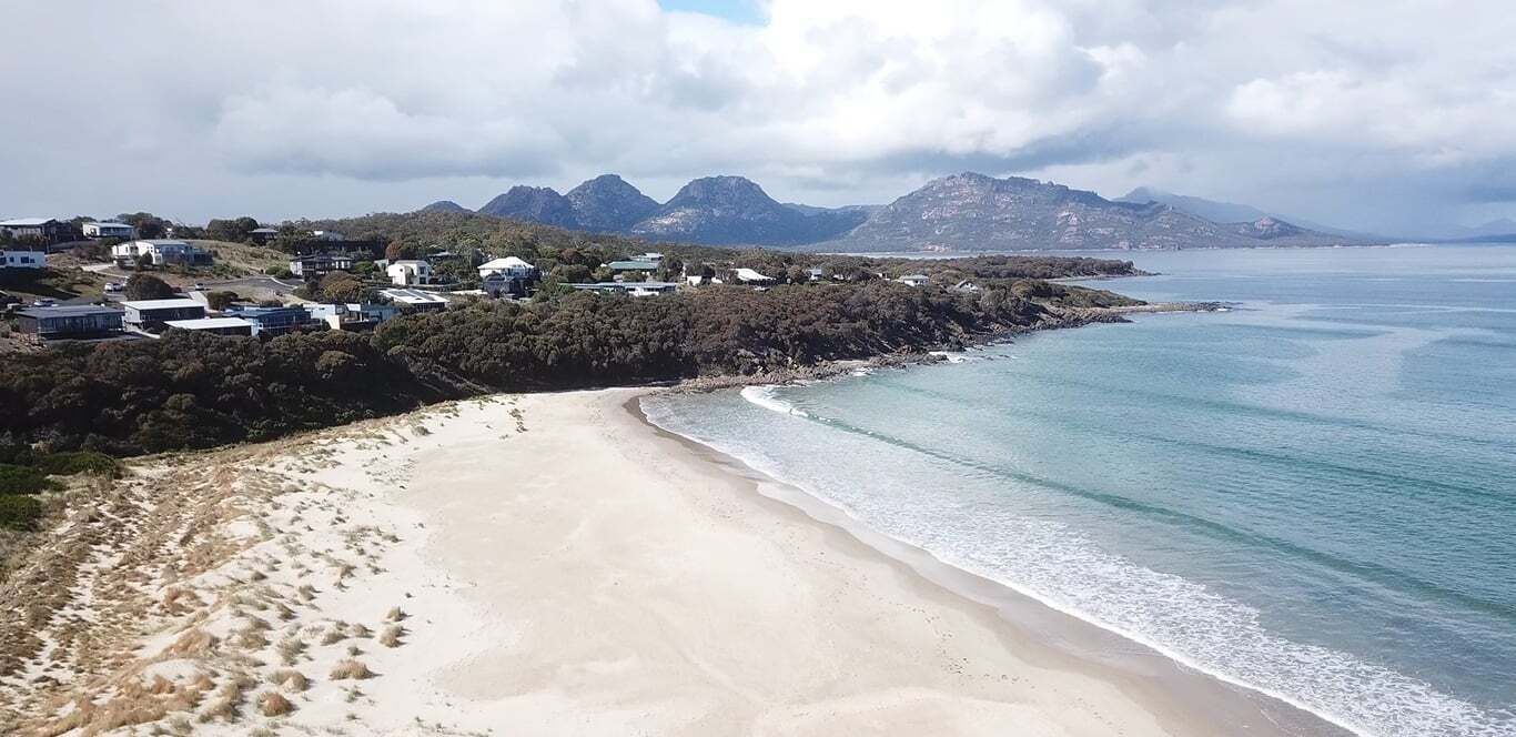 A coastal landscape with a sandy beach, a clear view of the sea, and a backdrop of mountains.