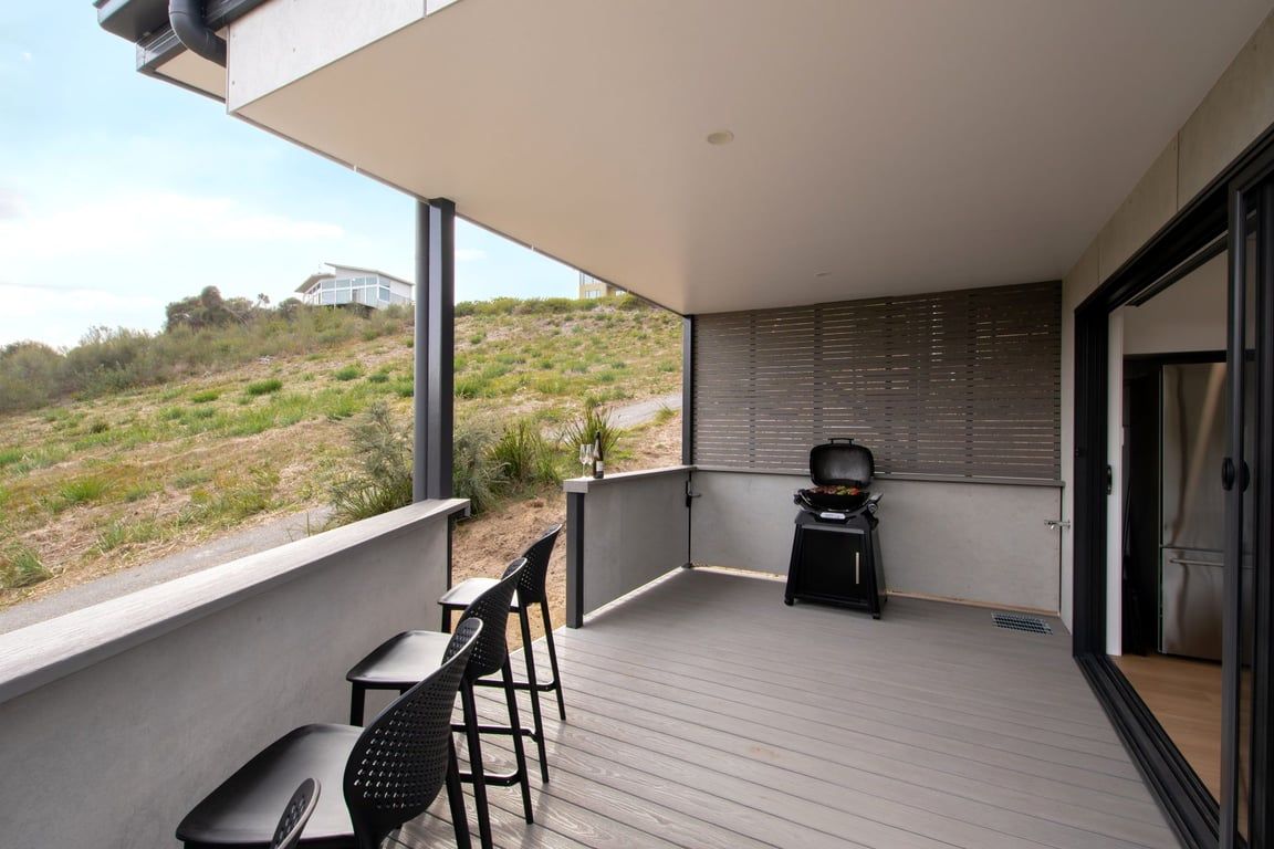 Een balkon met een tafel, stoelen, een barbecue en uitzicht op een heuvel.