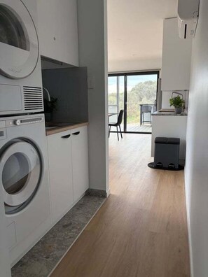 A modern kitchen with built-in appliances, a dining area with a view, and a large window. - Wave Front - Freycinet Holiday Houses (COLES BAY)