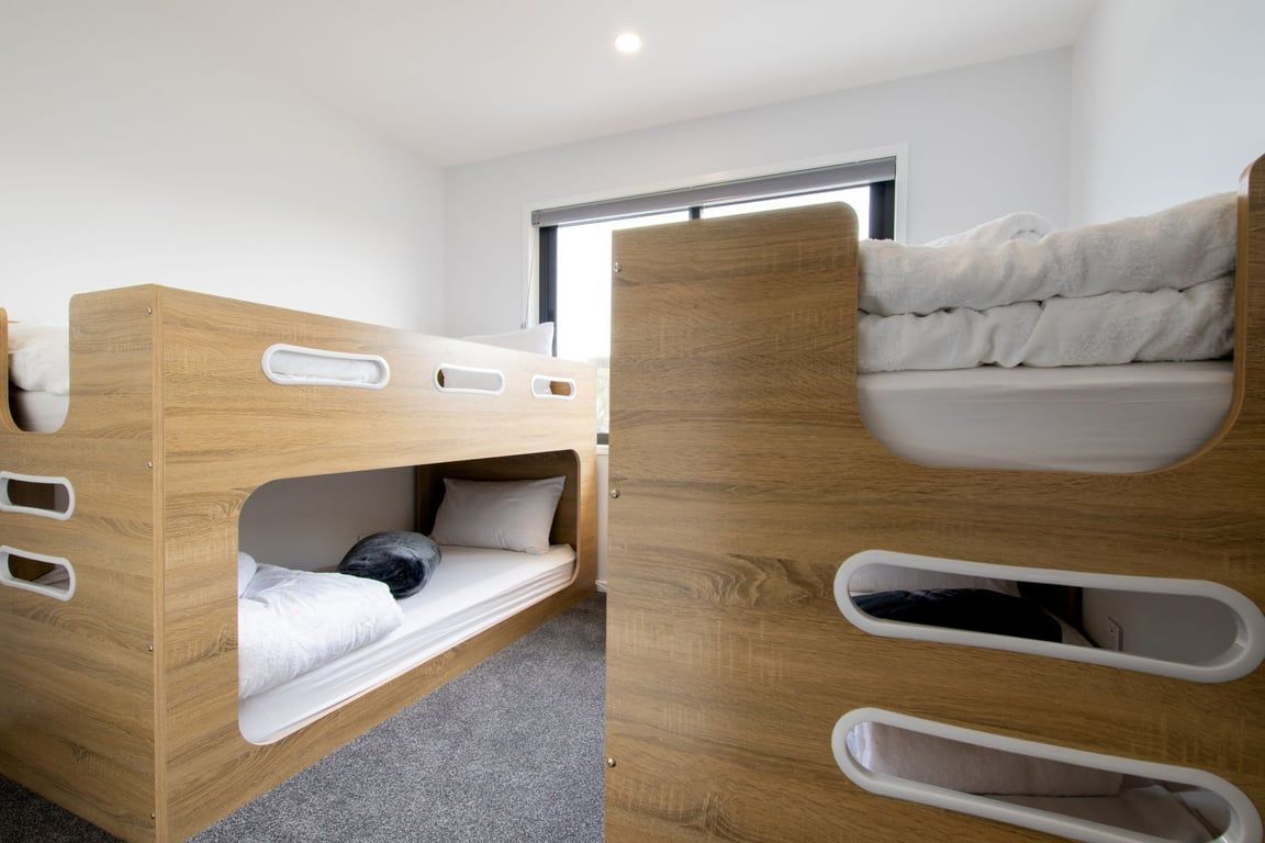 Een kamer met twee houten stapelbedden, een raam en een deur.