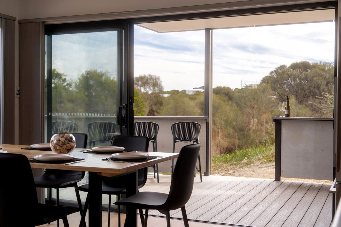 A dining area with a table set for four, chairs, and a view through a glass door to the outdoors.