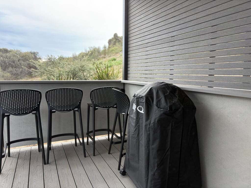 A balcony with three black chairs and a barbecue grill covered with a black cloth.