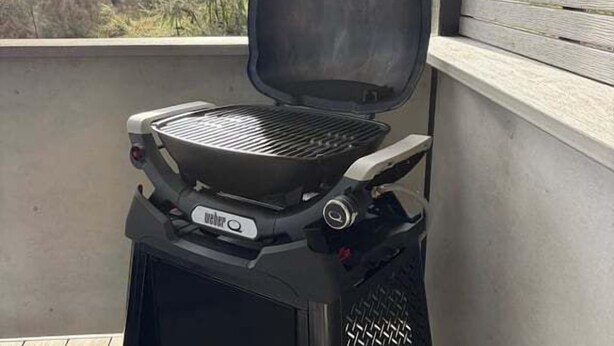Ein tragbarer Grill auf einem Balkon mit Blick auf Bäume und Himmel.