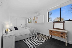 A bedroom with a bed, bedside table, dresser, and a window with a view.