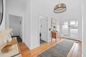A room with a wooden floor, a grey rug, a wooden dresser, a mirror, and a hanging light fixture.