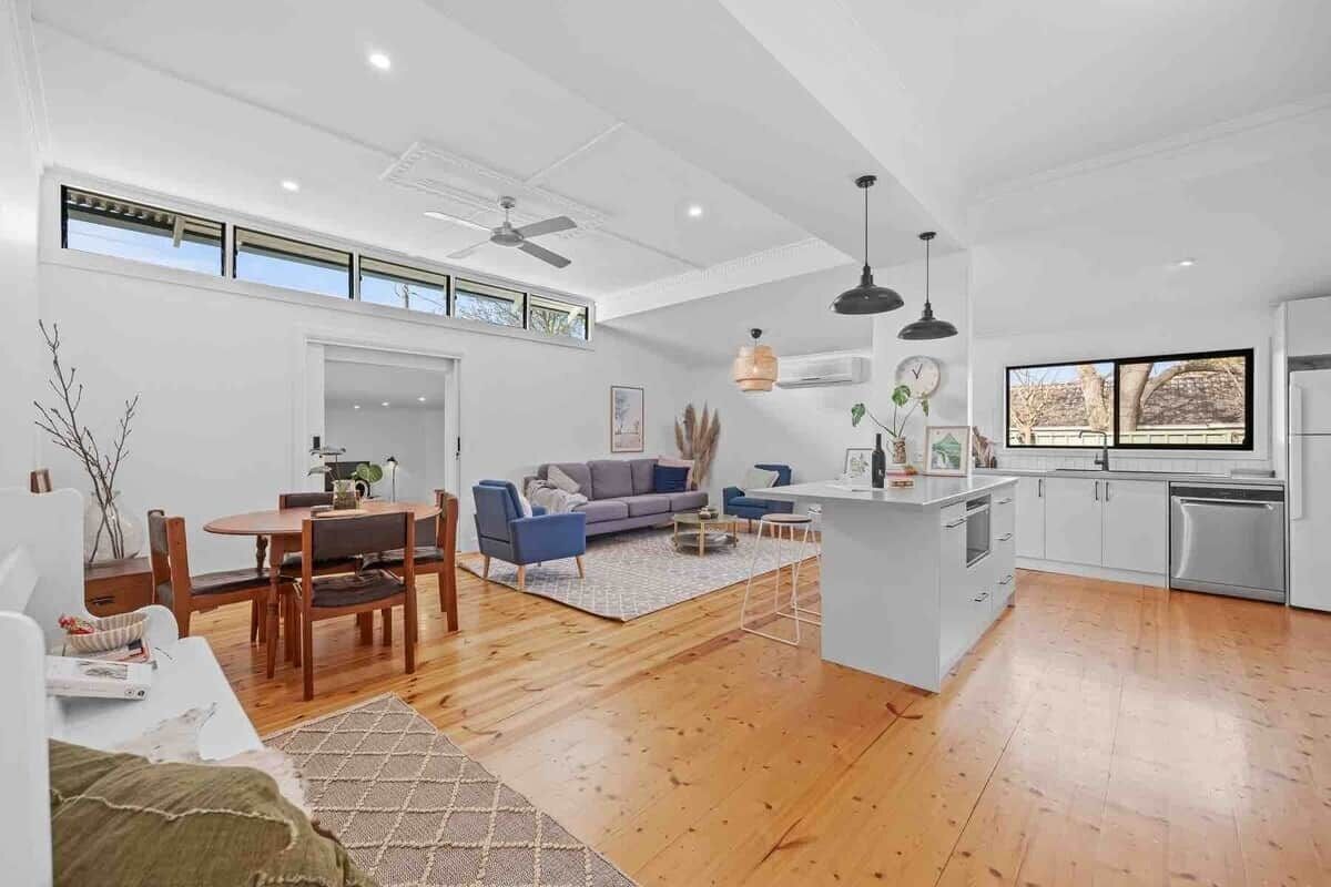 A spacious living area with a dining table, sofas, and a kitchen with white cabinets and a large window.