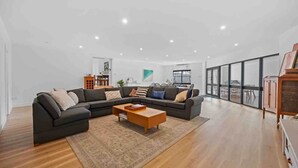 A modern living room with a sectional sofa, a wooden coffee table, and a large window offering a view of the outdoors. - House on Drummond - A large home close to the heart of central Ballarat (Ballarat Central)