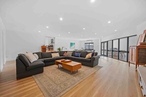 Ein modernes Wohnzimmer mit einer Eckcouch, einem Holztisch und einem großen Fenster mit Blick ins Freie.