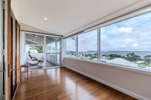 A spacious room with a large window offering a view of a coastal landscape. - Blue Horizon by The BNB Collection (Albany)