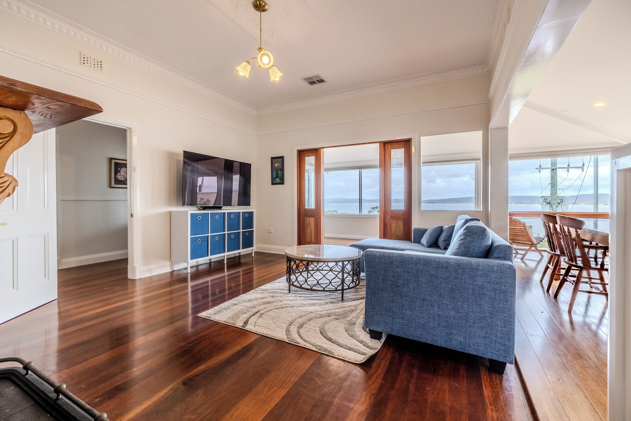 A spacious living room with a blue sofa, a TV, and a view of the sea.