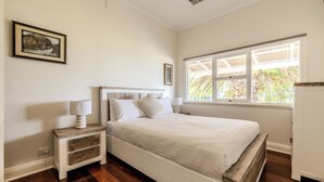 Un dormitorio con cama, mesitas de noche, una ventana con vistas y un cuadro colgado en la pared.