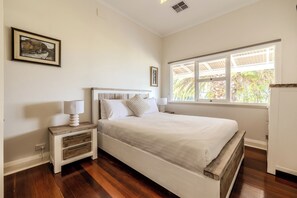 A bedroom with a bed, bedside tables, a window with a view, and a wall-mounted picture. - Blue Horizon by The BNB Collection (Albany)