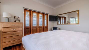 Quarto com uma cama grande, cômoda de madeira, televisão fixada na parede e janela com vista.