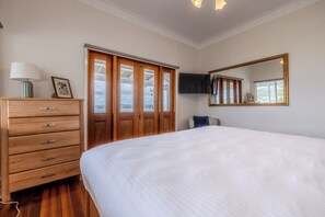 Un dormitorio con una cama grande, un aparador de madera, un televisor montado en la pared y una ventana con vistas.