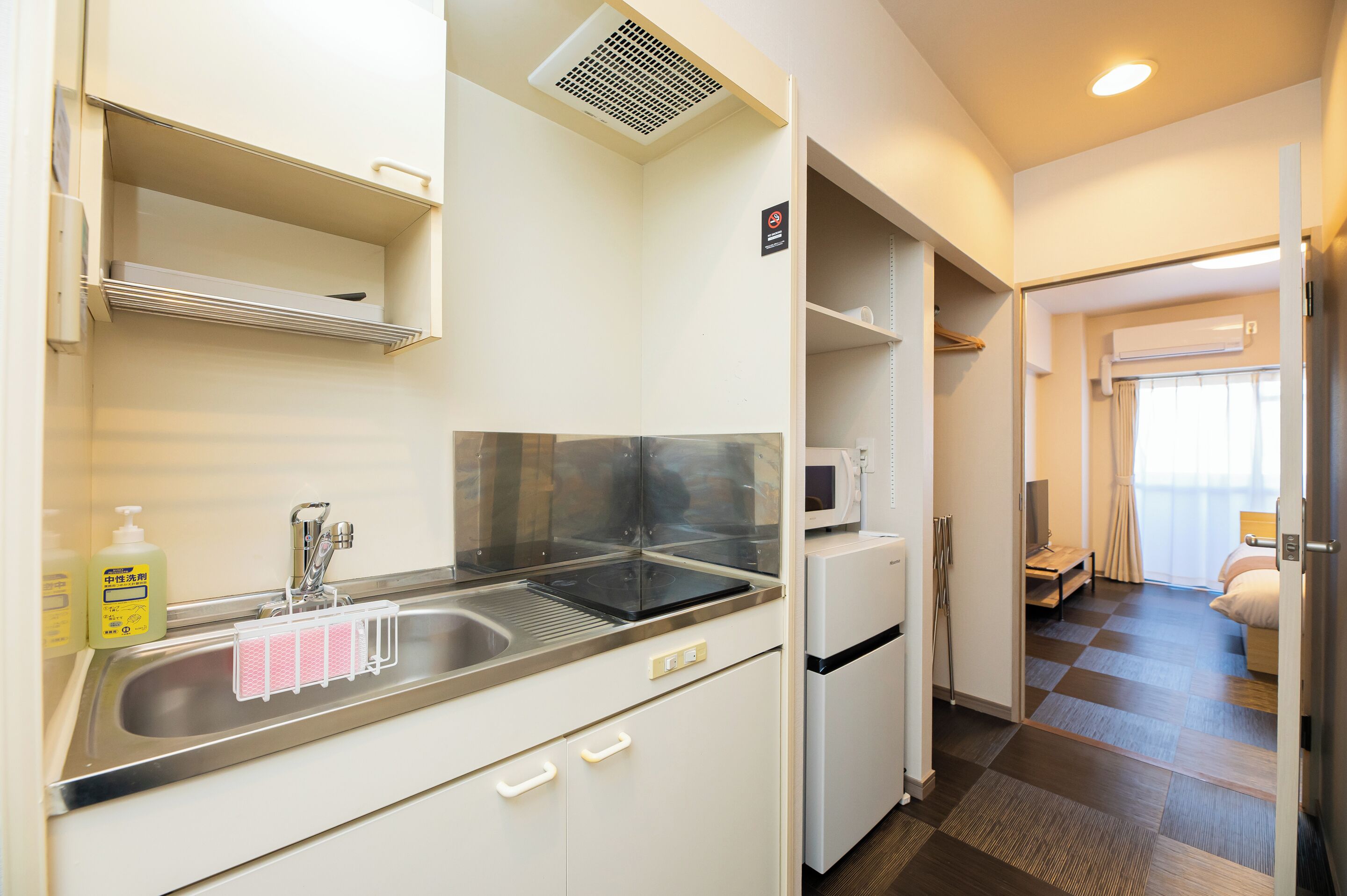 Cocina de hotel compacta con un lavamanos de acero inoxidable, un microondas y un refrigerador.