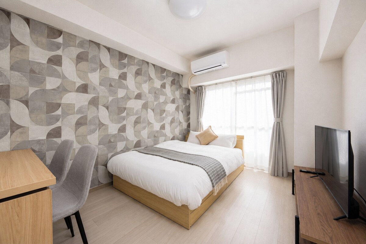 A modern hotel room with a large bed, a desk, a chair, a TV, and a window with curtains.