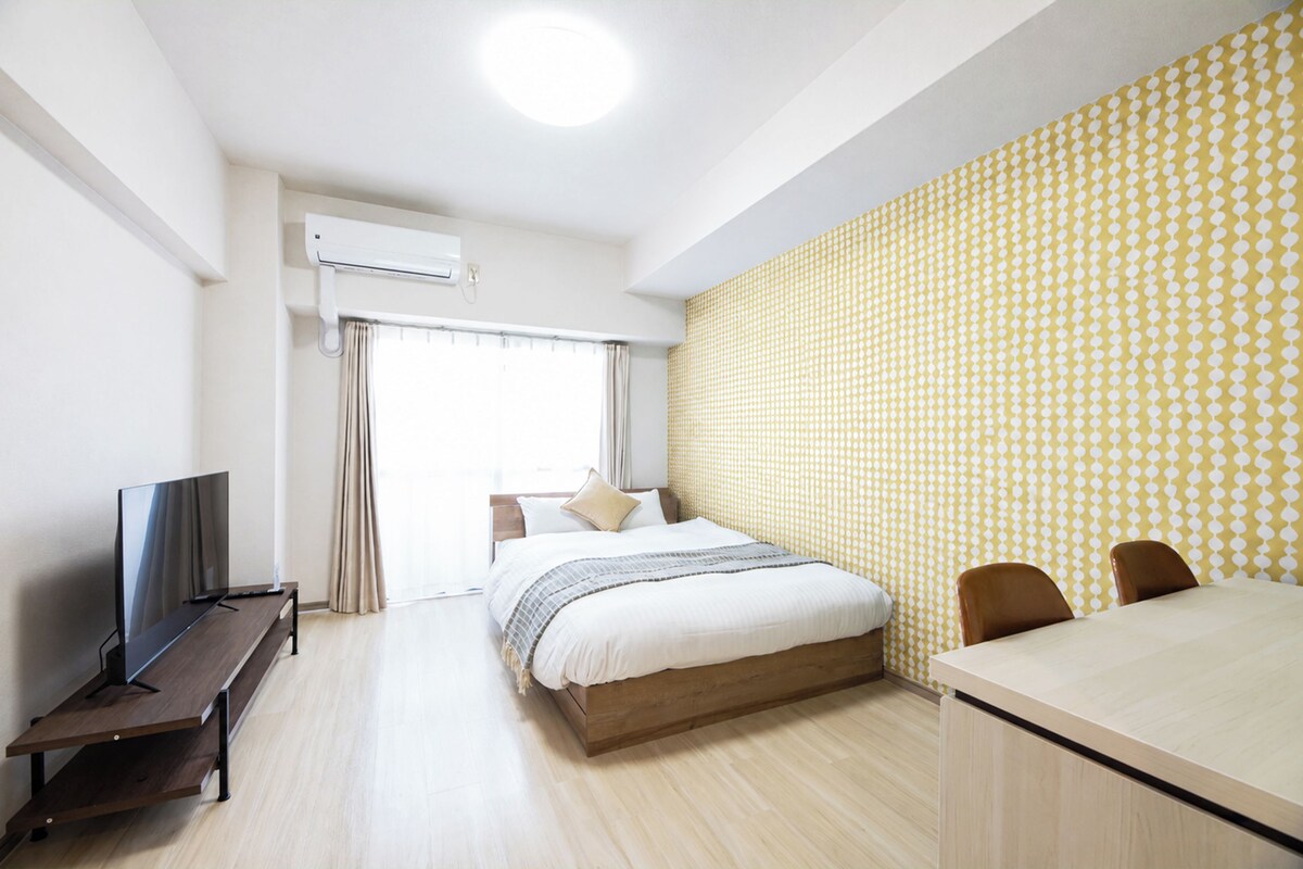 A hotel room with a bed, a desk, a TV, and an air conditioning unit.