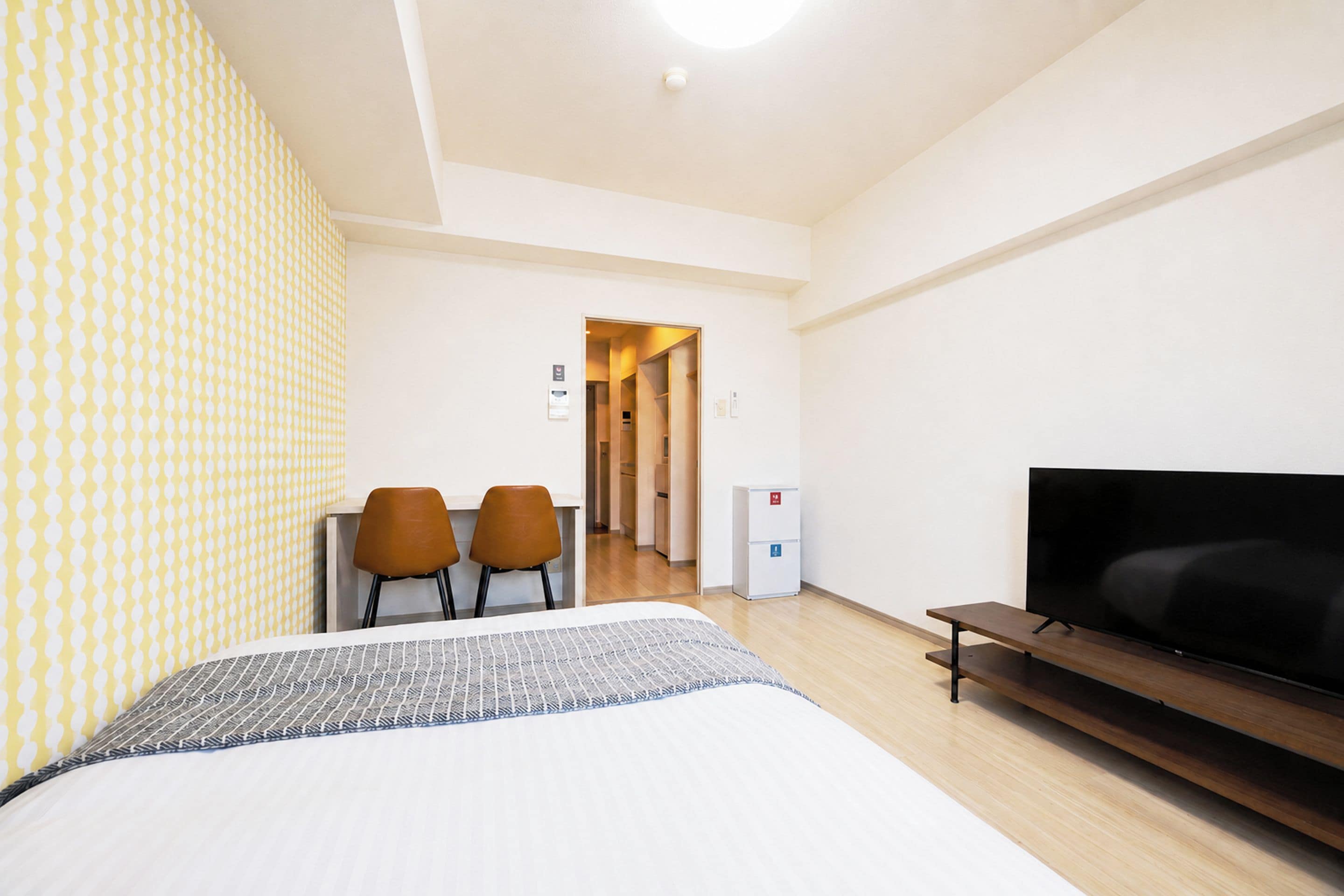 Une chambre d’hôtel avec un lit, une télévision, un bureau avec deux chaises et, au fond, une petite cuisine.