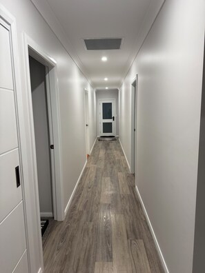 Un pasillo con paredes blancas, suelo de madera y una puerta al final.