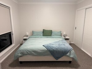 Un dormitorio con cama, mesitas de noche, ventana y armario.
