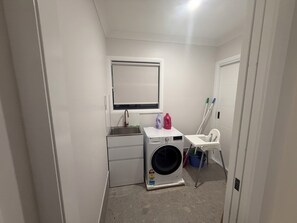 A compact laundry room with a washing machine, a small sink, and a drying rack.