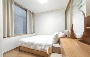 Un dormitorio con cama, cómoda de madera, espejo y ventana con cortinas.