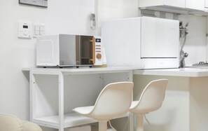 Eine Küche mit einer Mikrowelle, einem Kühlschrank und zwei weißen Stühlen.