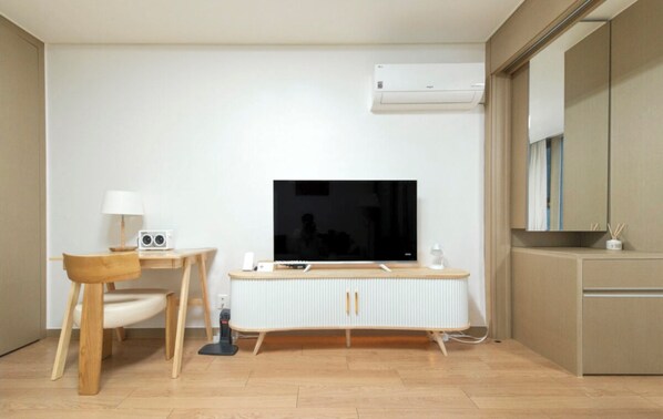 Ein kleiner, moderner Raum mit Fernseher, Schreibtisch mit Stuhl, Heizkörper und Spiegel.